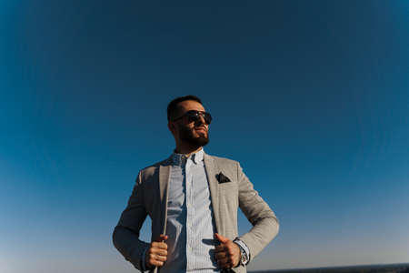 Handsome bearded arabian man in sunglasses on the blue sky background. Confident muslim business man. Arab man weared in gray coatの写真素材