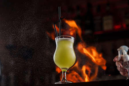Bartender sprinkles on illuminated glass with bright green cold cocktail on bar counter and makes fire flame over it.の写真素材