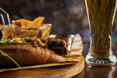Barbecue grilled hot dog and beer with yellow mustard and ketchup on wooden background. Hot dog sandwich with potato fries and sauces.の写真素材