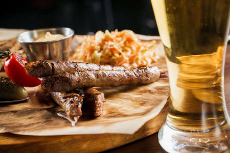Grilled sausages with beer and vegetables with pickled cucumber, cabbage salad sauce and bread on parchment, top view.の写真素材