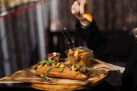 Barbecue grilled hot dog with yellow mustard and ketchup on wooden background. Hot dog sandwich with potato fries and sauces.の写真素材