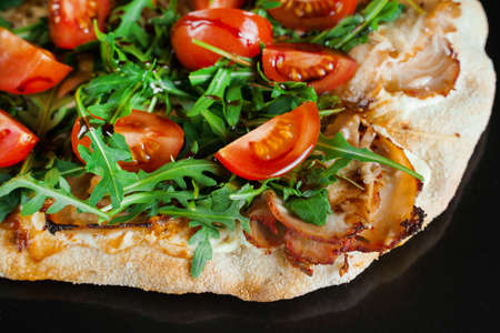 Pinsa romana gourmet italian cuisine on black background. Scrocchiarella traditional dish. Food delivery from pizzeria. Pinsa with meat, arugula, tomatoes, cheese.の写真素材