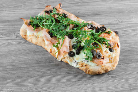 Pinsa romana gourmet italian cuisine on gray wooden background. Scrocchiarella traditional dish. Food delivery from pizzeria. Pinsa with meat, arugula, olives, cheese.の写真素材