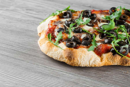 Pinsa romana gourmet italian cuisine on gray wooden background. Scrocchiarella traditional dish. Food delivery from pizzeria. Pinsa with meat, arugula, olives, cheese.の写真素材