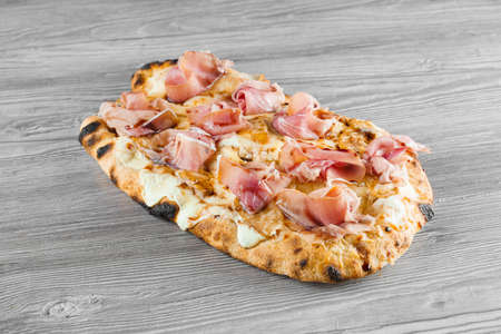 Scrocchiarella with pear, cheese, prosciutto on gray wooden background. Pinsa romana gourmet italian cuisine. Food delivery from pizzeria. Junk foodの写真素材