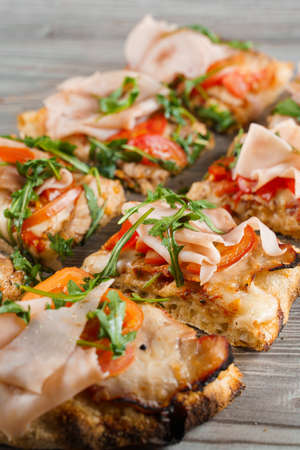 Pinsa romana cut into pieces portions for one person. Food delivery from pizzeria. Pinsa with meat, arugula, cheese. Scrocchiarella gourmet italian cuisine on gray wooden background.の写真素材