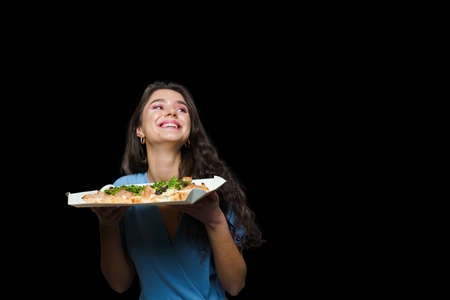 Woman courier with pinsa romana gourmet italian cuisine on black background. Holding scrocchiarella traditional dish. Food delivery from pizzeria. Pinsa with meat, arugula, olives, cheese.の写真素材