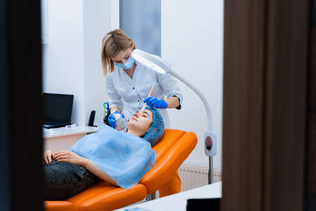 Dermatologist smears black mask on face for laser photorejuvenation and carbon peeling. Dermatology...