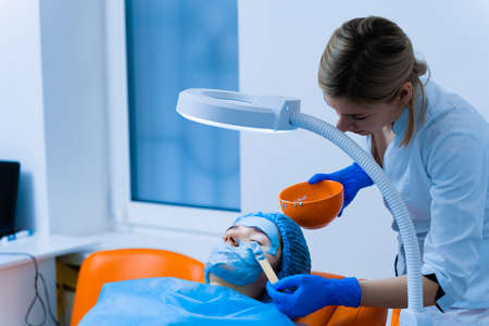 Alginate moisturizing mask for face and skin of young girl. Spa procedure for rejuvenation. beautician smears blue mask. Dermatology in medical clinicの写真素材