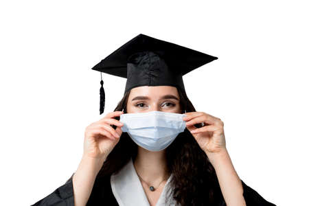 Graduate girl in medical mask at coronavirus covid-19 period. Woman with master degree in black graduation gown and cap. Distance learning online. Study at home. Graduation from college.の写真素材