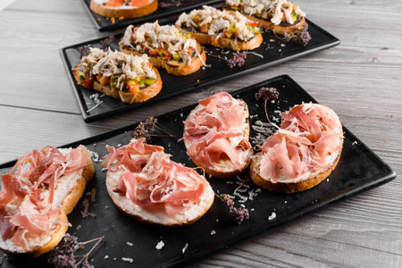 Charcuterie and cheese board with cured meat and different types of cheese. Smoked meat ot the black plate. Food board with tasty parmesan, dorblu, soft cheese, camembert.の写真素材
