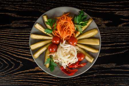 Assortment of pickles, cherry tomatoes, chili with carrots, onions and parsley on a gray plate on a dark wooden table. Top view.の写真素材