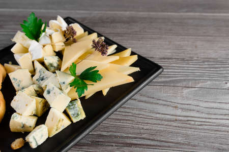Cheese food board with delicous cheeses, walnuts. Parmesan, jam, dorblu on the black plate. Food appetizer from restaurantの写真素材