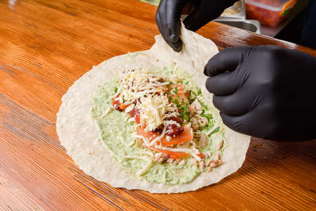 Burrito making process. The chef wraps stuffed pita on a wooden table. Mexican dish.の写真素材