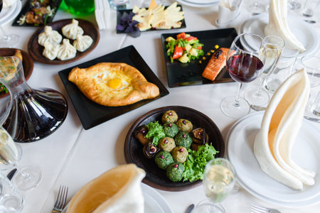 Assortment of dishes phali, khachapuri, salmon, khinkali, vegetables table setting bowl with wine, glasses, dishes, napkinsの写真素材