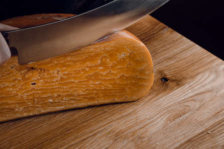 Slicing aged cheese parmesan with crystals using a cheesy dutch knife. Hard cheese with knife on dark background. Snack tasty piece of food for appetizerの写真素材