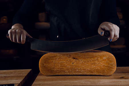 Slicing aged cheese parmesan with crystals using a cheesy dutch knife. Hard cheese with knife on dark background. Snack tasty piece of food for appetizerの写真素材