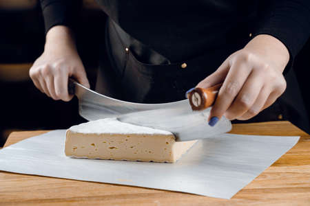 Brie soft white cheese from cow milk. Slicing brie on the wooden table. Organic delicious foodの写真素材