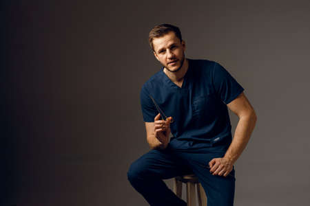 Handsome doctor with surgical scissors and needle holder. Confident man holding medical equipment in...