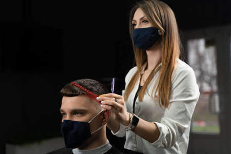 Barbershop service at virus period. Woman barber making hair for handsome man. Using mask