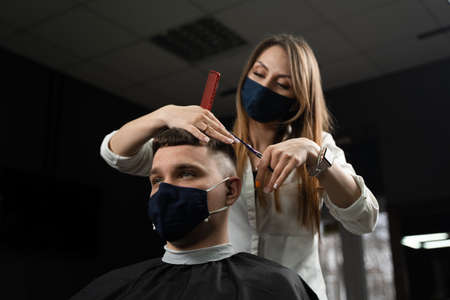 Barbershop service at virus period. Woman barber making hair for handsome man. Using maskの写真素材