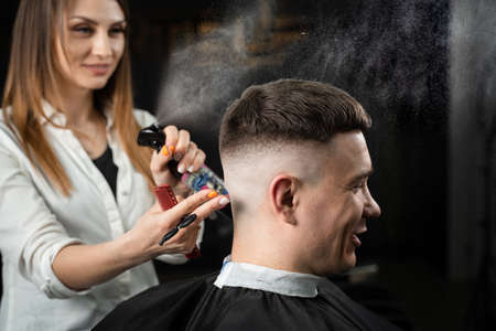 Woman barber making hairstyle in barbershop using clipper. Hairdresser cutting hair of handsome manの写真素材