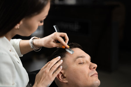 Straight razor cut man hair in barbershop. Attractive woman barber making hairstyle for handsome manの写真素材