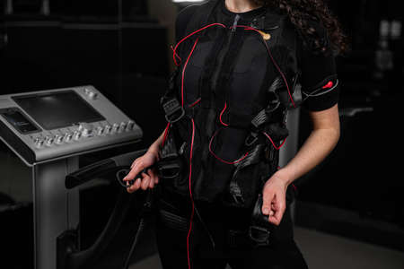 Girl in EMS suit in gym. Sport training in electrical muscle stimulation suit. Making physical exercises.の写真素材