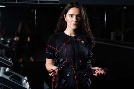 Girl in EMS suit in gym. Sport training in electrical muscle stimulation suit. Making physical exercises.の写真素材