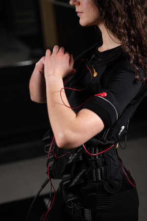 Girl in EMS suit in gym. Sport training in electrical muscle stimulation suit. Making physical exercises.の写真素材