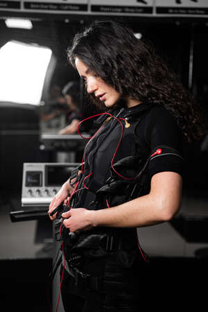 Girl in EMS suit in gym. Sport training in electrical muscle stimulation suit. Making physical exercises.の写真素材