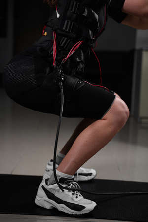 Girl in EMS suit in gym. Sport training in electrical muscle stimulation suit. Making physical...