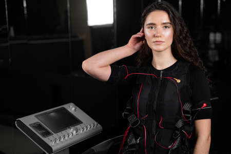Girl in EMS suit in gym. Sport training in electrical muscle stimulation suit. Making physical...
