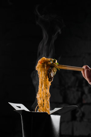 Steaming rice noodles in wok box on black background. Fast food delivery service. Takeaway chinese street meal. Udon in black food containerの写真素材