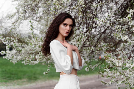 Portrait of young woman in the garden. Attractive girl weared white dress posing near blooming treesの写真素材