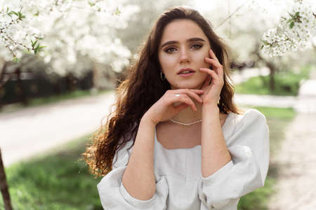 Lovely girl near blooming trees in the park. Outdoor walking in at sunny day. Lifestyle of young...