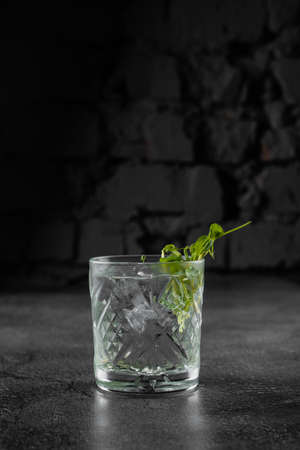 Glass with drink, ice on gray background. Alcohol cocktail decorated microgreenの写真素材
