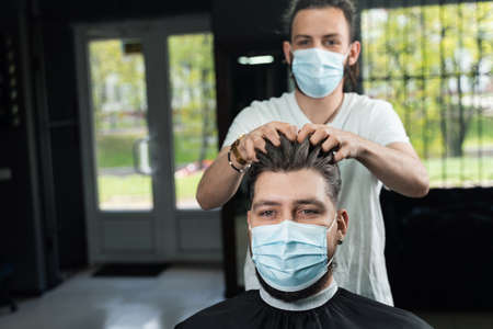 Hair styling with wax for a bearded man in a medical mask. The work of the barbershop in quarantineの写真素材