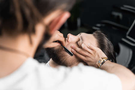 Straight razor cut mans beard in barbershop. Barber man making hairstyle for handsome manの写真素材