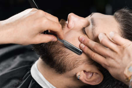 Straight razor cut mans beard in barbershop. Barber man making hairstyle for handsome manの写真素材