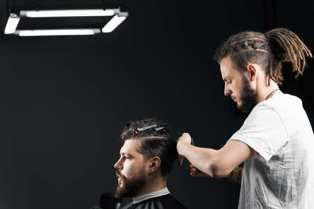 Barber making hairstyle for confident bearded hipster. Advertising for barbershop and men's beauty salonの写真素材