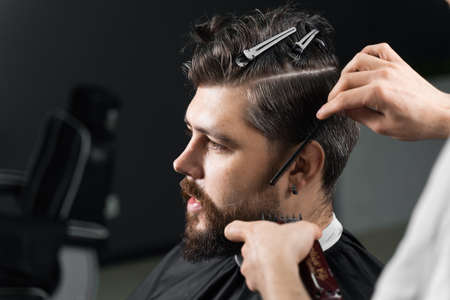 Barber making hairstyle for confident bearded hipster. Advertising for barbershop and men's beauty salonの写真素材