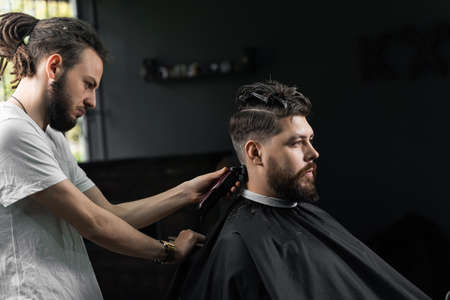 Low fade machine haircut for handsome bearded man in barbershop. Barber with dread locks making hairstyle with a smooth transitionの写真素材