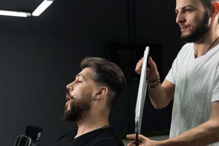 Happy and surprised bearded man looking in mirror in barbershop. Showing result of low fade machine...