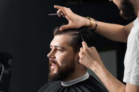 Barber making hairstyle for confident bearded hipster. Advertising for barbershop and men's beauty salonの写真素材