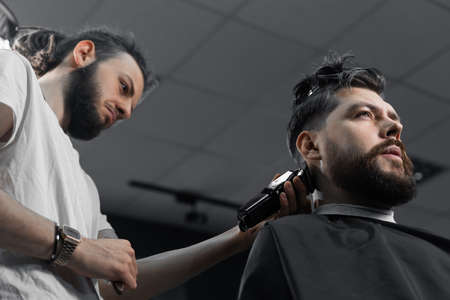 Low fade machine haircut for handsome bearded man in barbershop. Hair cut with a smooth transition