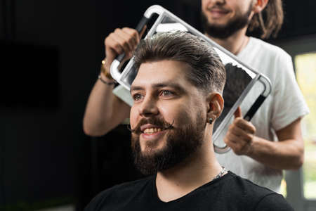 Happy and surprised bearded man looking in mirror in barbershop. Showing result of low fade machine hair.の写真素材