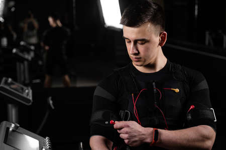 Handsome trainer in EMS suit with red wires for electro impulse stimulation for body. Training in gymの写真素材