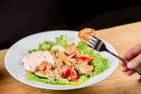Salad with shrimps, quinoa, tomatoes, peppers, cucumber, lettuce, mayonnaise on white round plate on wooden tableの写真素材