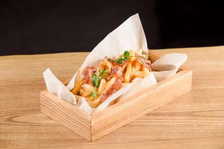 French fries with fried bacon on parchment in wooden box on the tableの写真素材